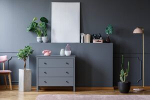 Plant next to grey cabinet with pink phone in living room interi